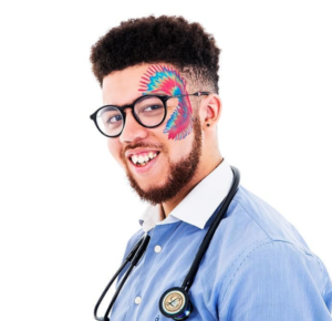 Head and shoulders shot of Dr Rhys Dore. He wears a blue shirt, with a white collar, and a stethoscope around his neck. He has a colourful rainbow pattern painted from his left forehead down to his left upper cheek. He is smiling.